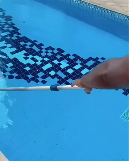 Limpeza de piscina com a peneira de cabo longo, na borda de pastilhas azuis